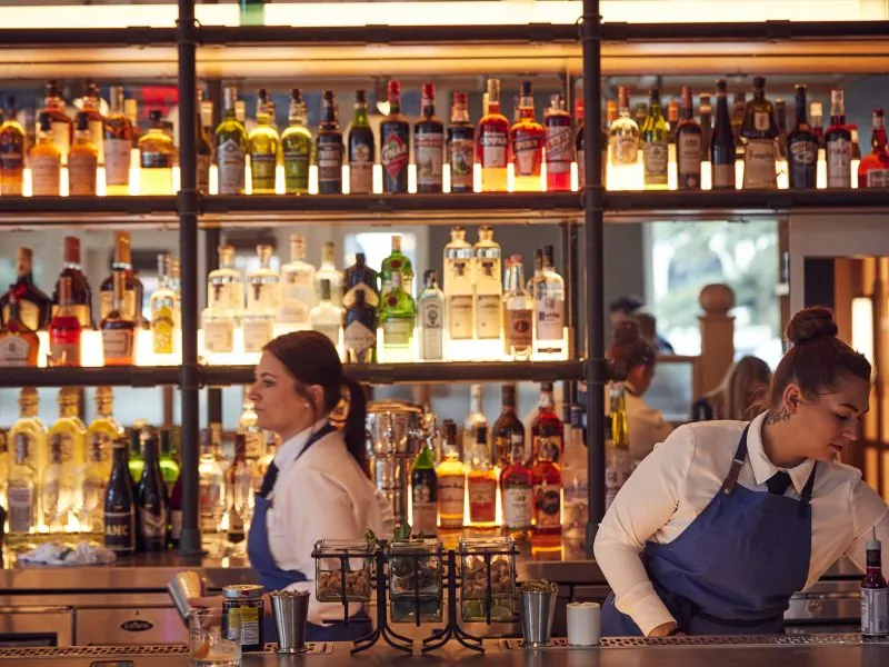 Bartenders at work behind the backlit bar at Pendant Terrace & Rooftop Bar