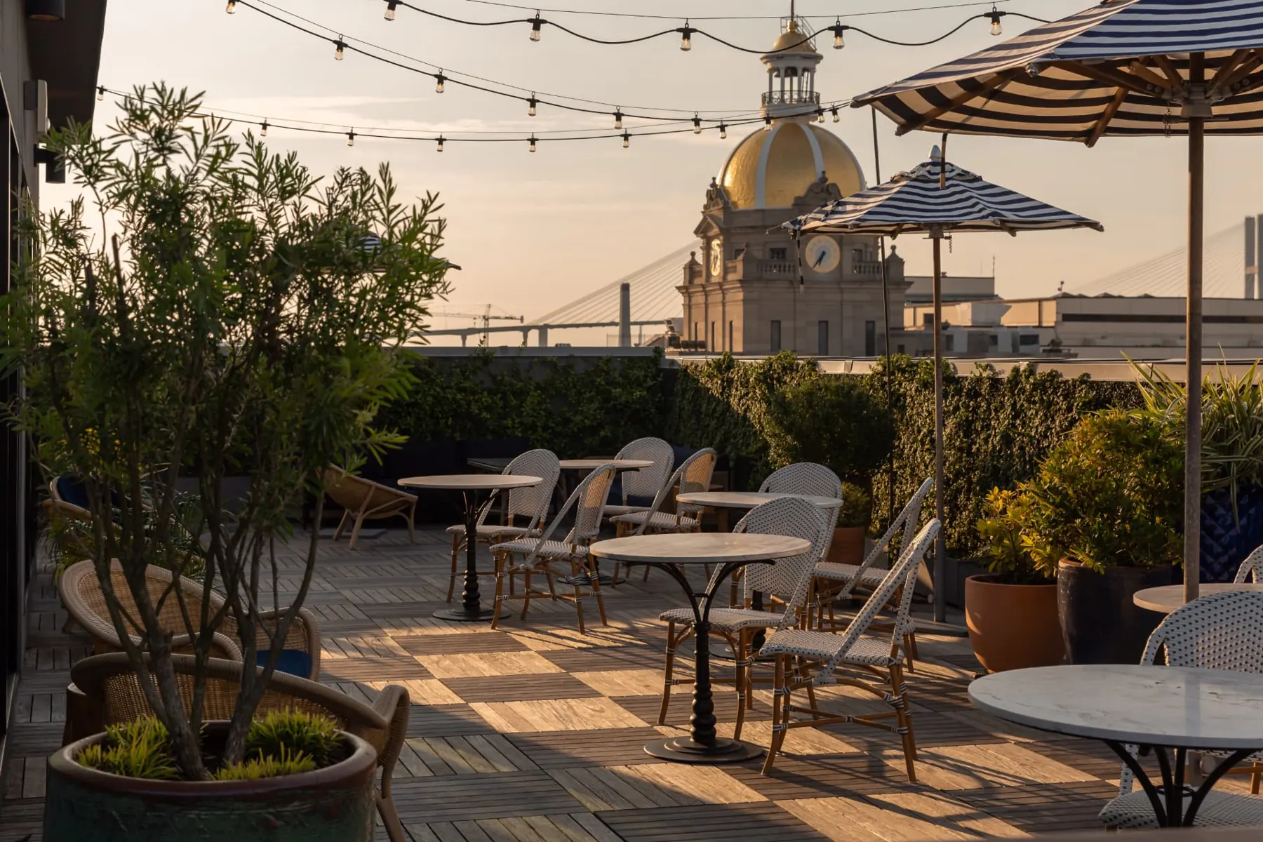Rooftop terrace with string lights and striped umbrellas beside City Hall's gold dome