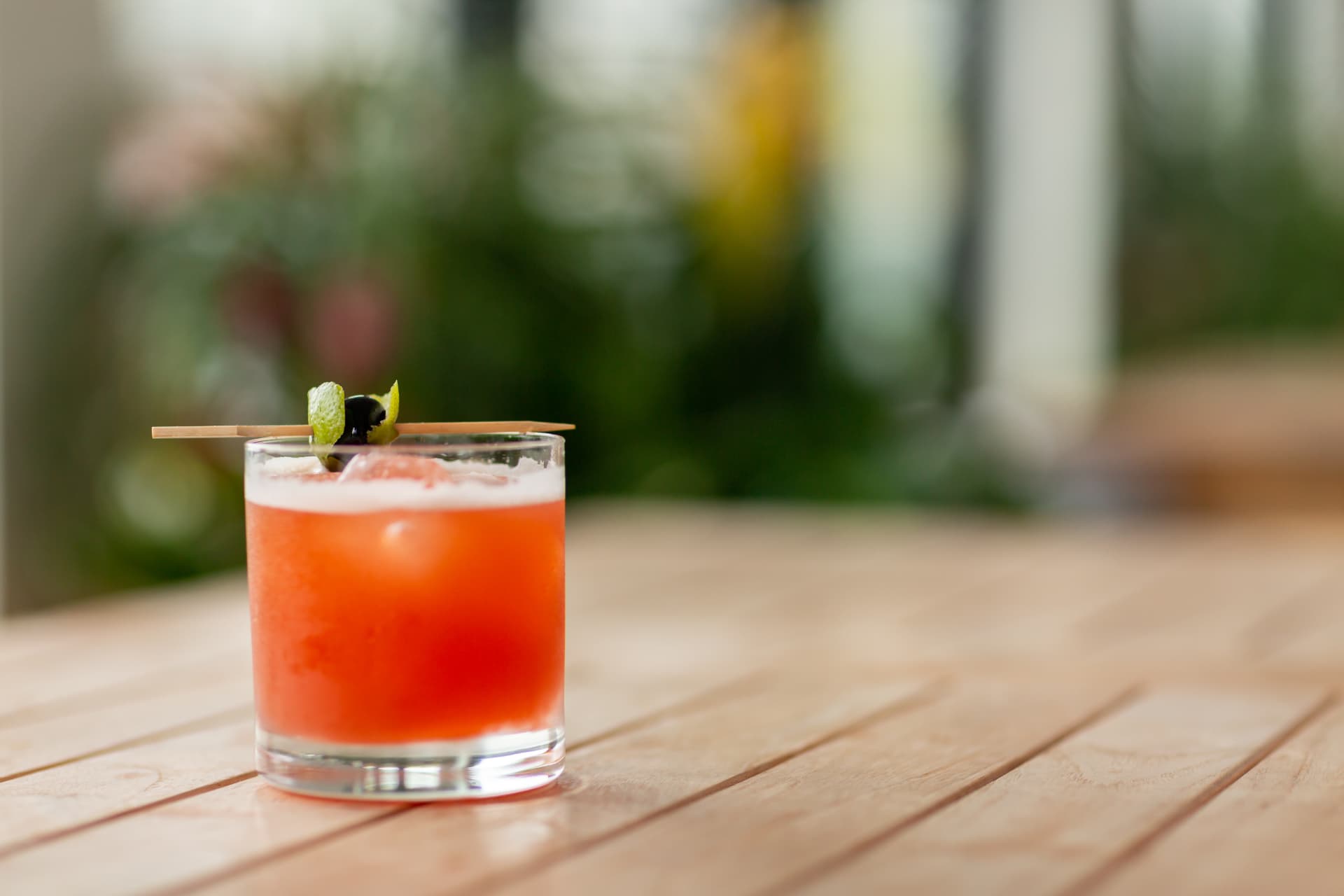 Red cocktail on a wood table with a lime garnish