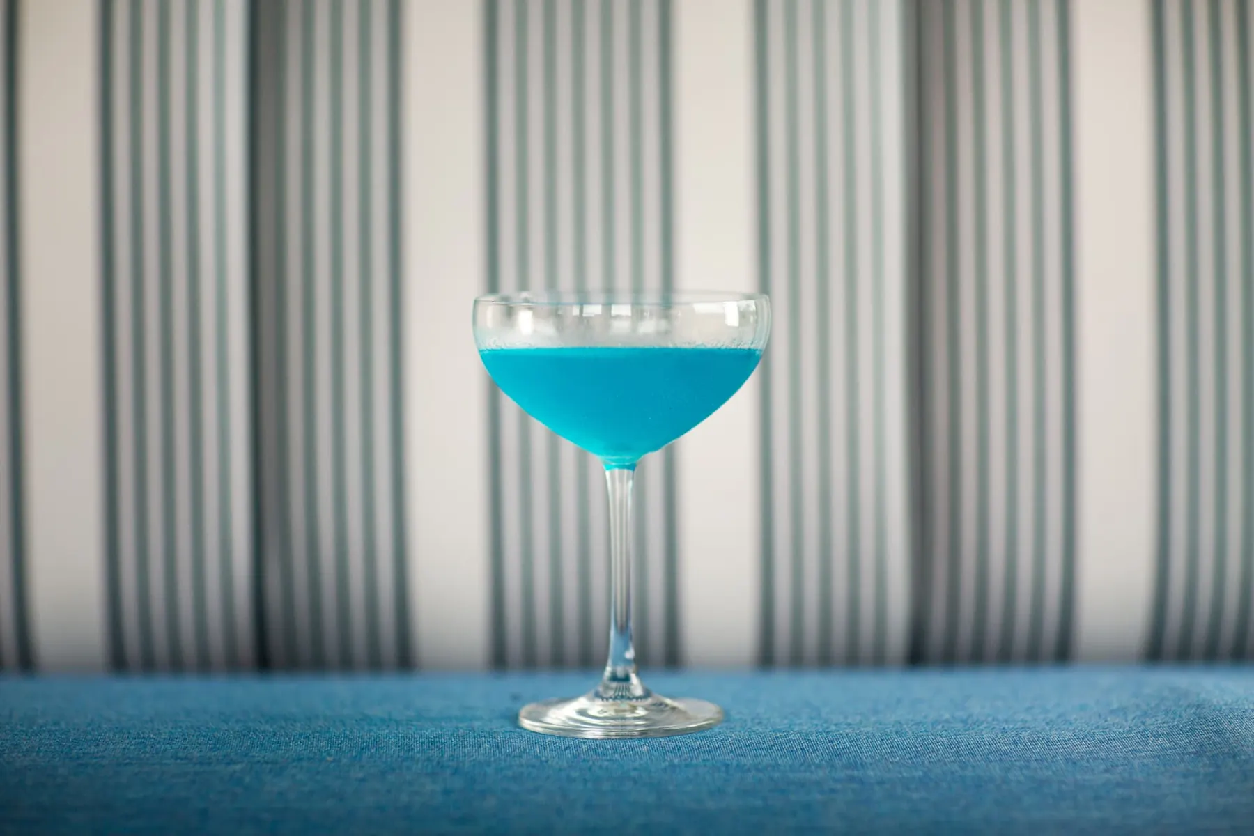 Blue cocktail in a coupe against striped banquettes